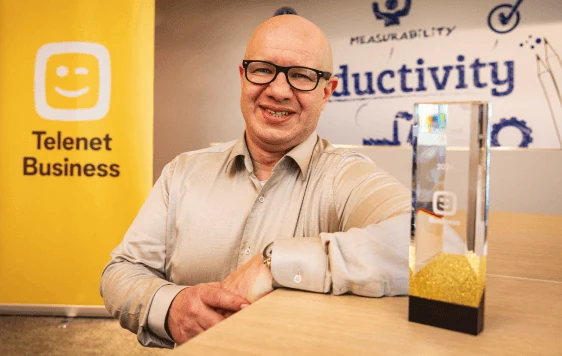 Ringo Deloof aan tafel naast de trofee van De Slimste Cyberexpert 2024, met een banner van Telenet Business